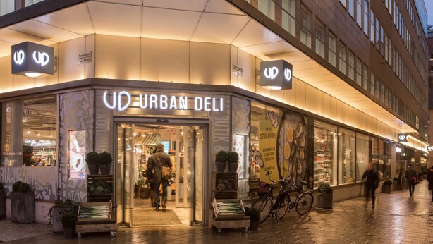 Exterior de Urban Deli con fachada moderna, grandes ventanales y una bicicleta estacionada afuera.