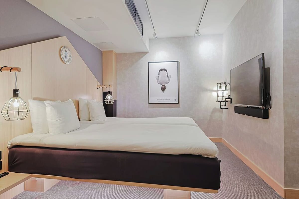 Una habitación de hotel moderna con una cama grande, un televisor de pantalla plana en la pared y una lámpara de pared original.