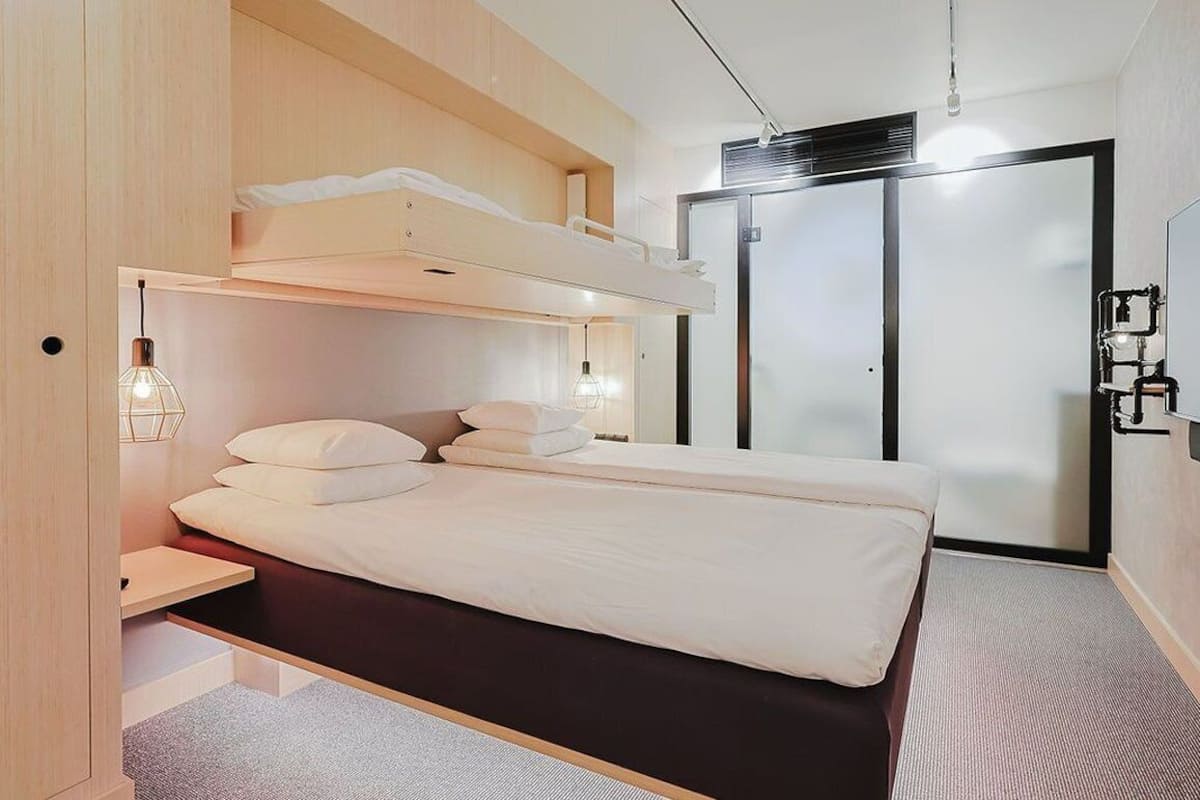 Un dormitorio moderno con una cama litera, una mesita de noche, una lámpara y un armario.