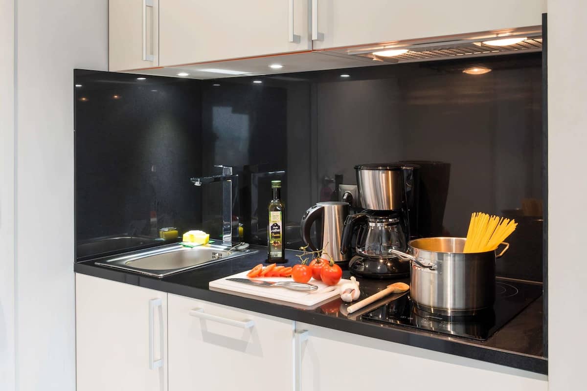 Uma cozinha moderna com bancada preta, eletrodomésticos de aço inoxidável e armários brancos.