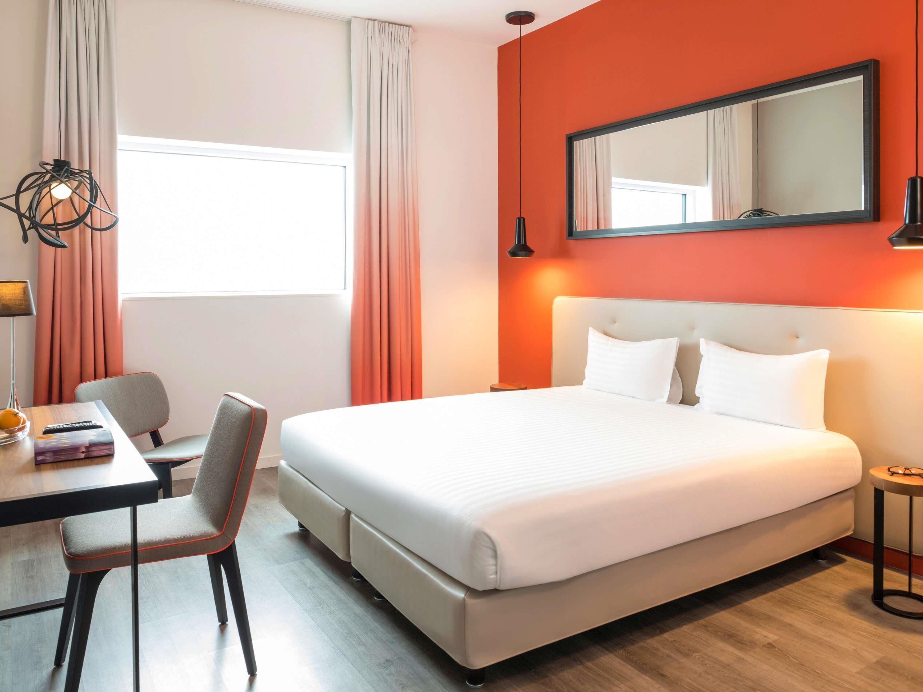 Hotelkamer met een bed, bureau met stoel, een tafeltje, lamp en raam met gordijnen.