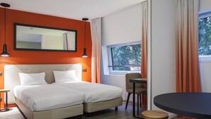 Une chambre d’hôtel moderne avec un lit double, une petite table, une chaise et une fenêtre avec des rideaux.