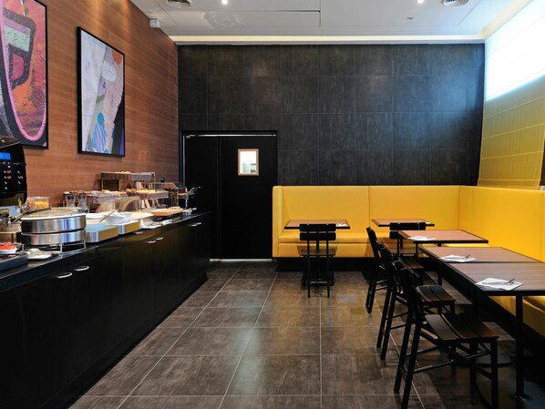 A modern restaurant with a black and yellow color scheme, featuring a buffet area, seating with tables and benches, and a dark tiled floor. - Adagio Paris 19e Cité de la Musique (Paris)