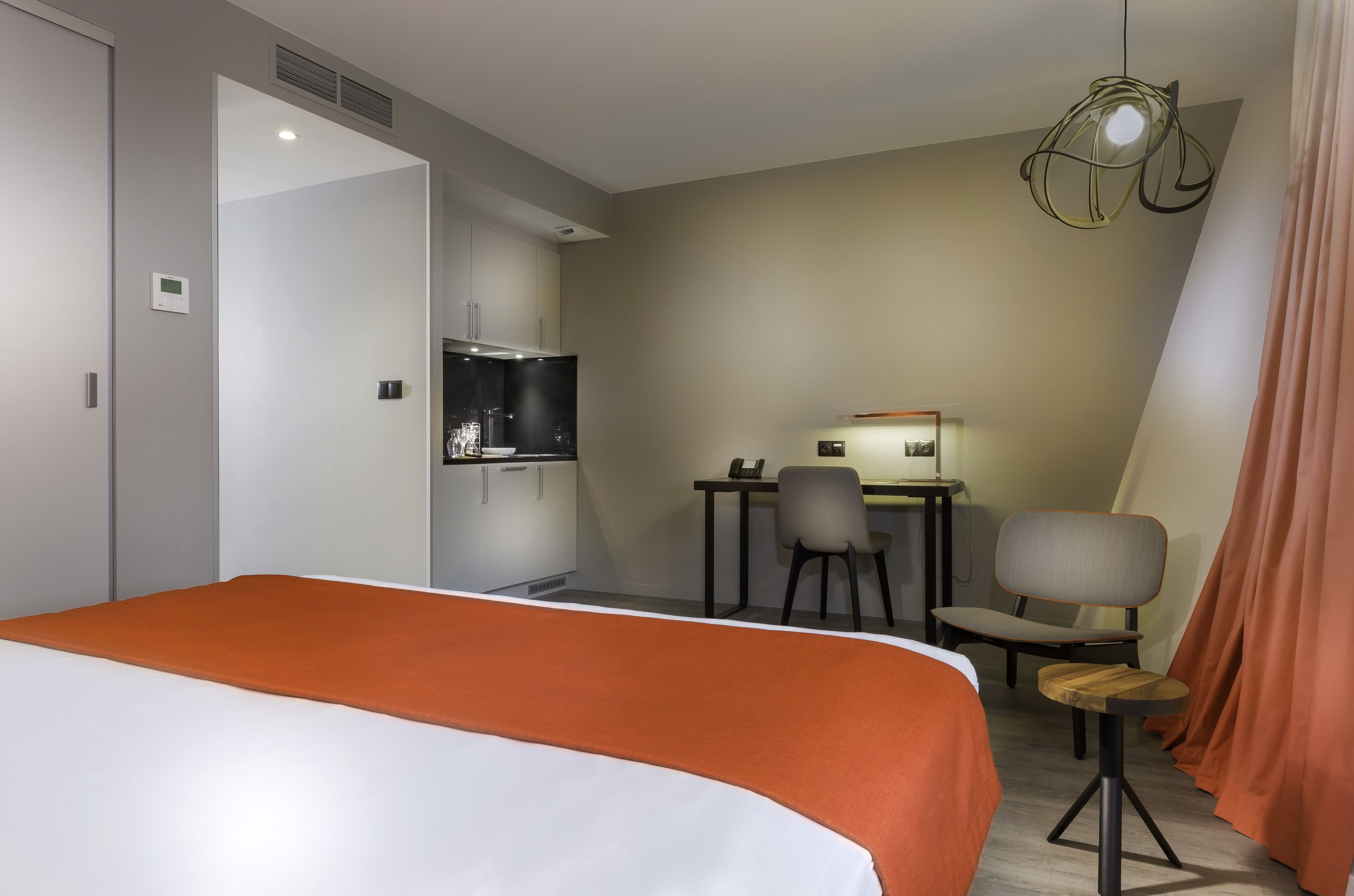 A hotel room with a bed, a desk with chairs, a television, and a dining area.