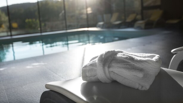 A poolside area with a towel on a chair, a clear view of the pool, and a sunlit background. - Prazer da Natureza Resort & SPA (Caminha)