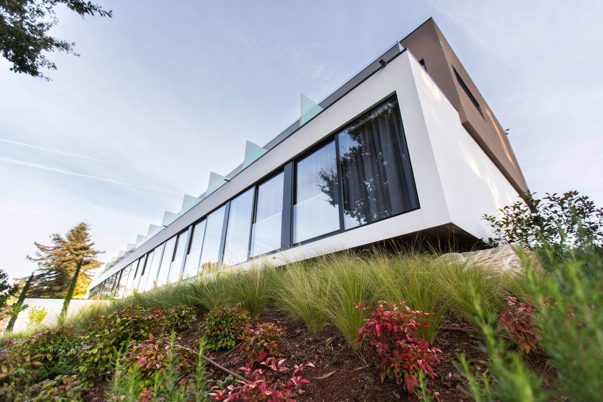 A modern building with large windows and a sloped roof, surrounded by greenery.