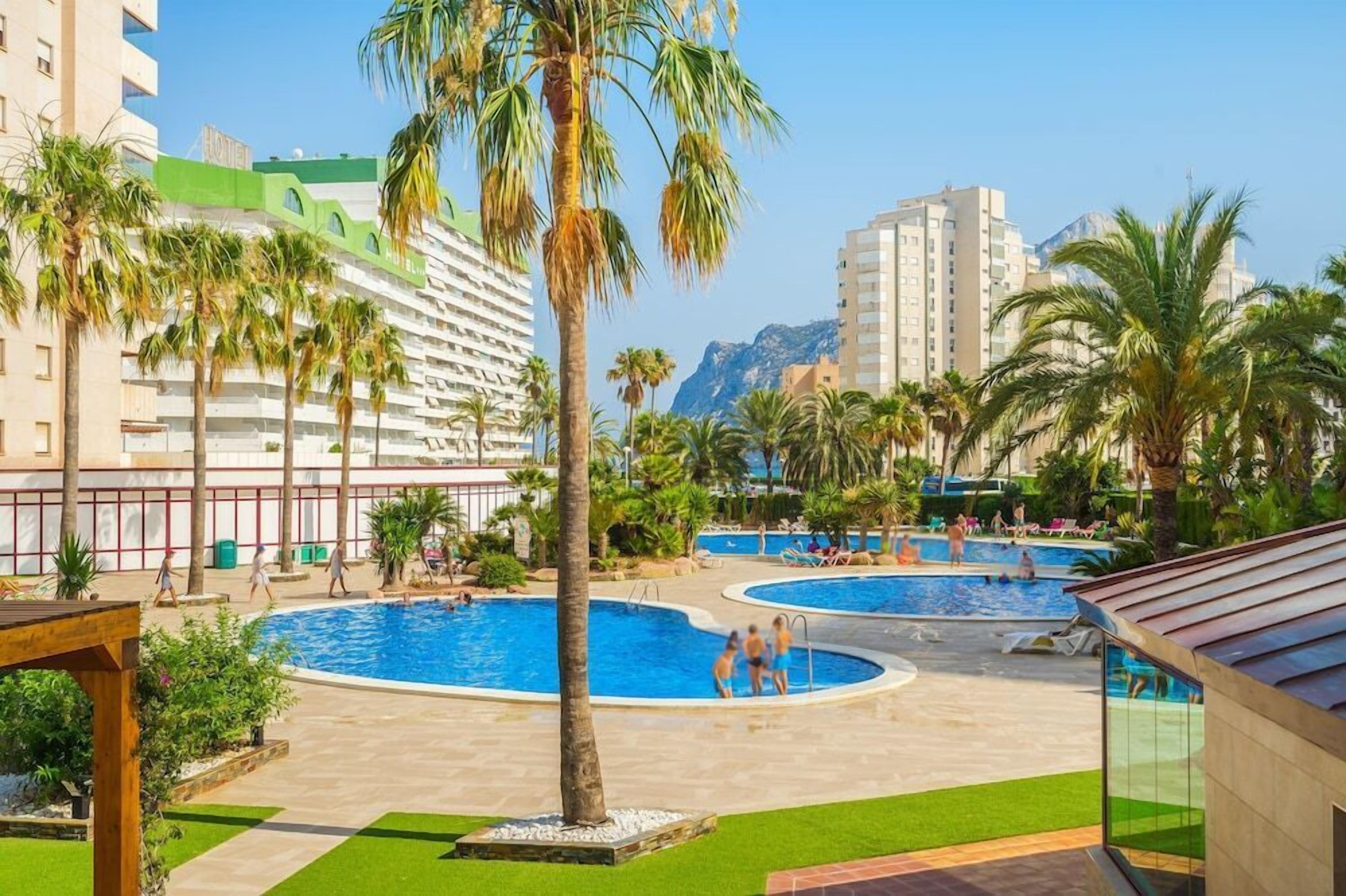 Zona de piscina en un resort con varias piscinas, palmeras y una vista de la montaña al fondo.