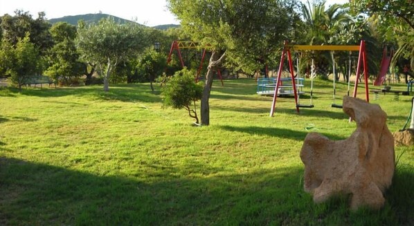 A park with a grassy area, a swing set, and a stone sculpture. - Il Castello (Villaputzu)