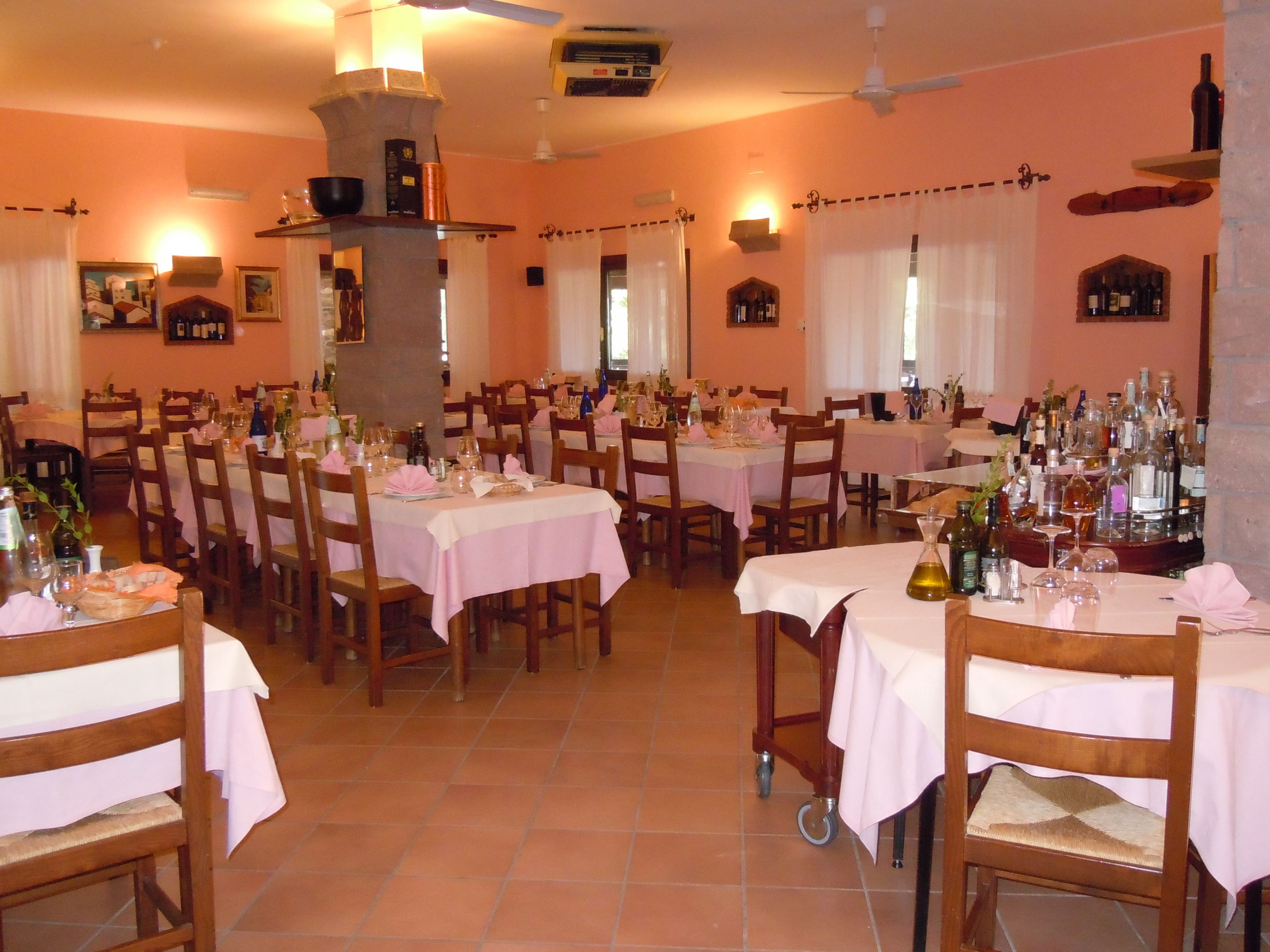 A restaurant with multiple tables set for dining, chairs, and a variety of bottles and glasses on the tables.