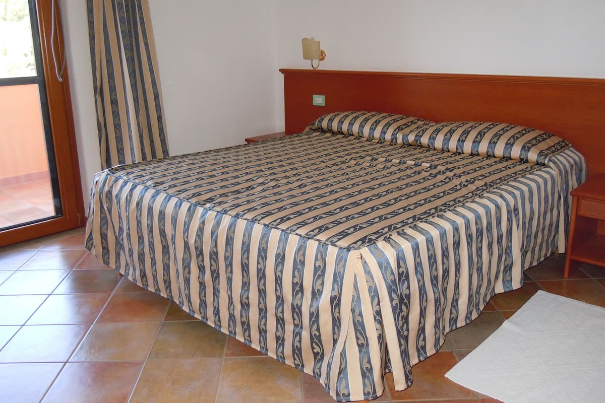 A bedroom with a large bed, a wooden headboard, a nightstand, and a window with curtains.