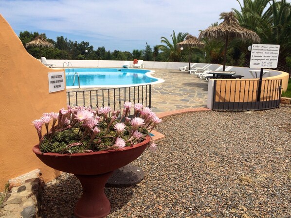 A pool area with lounge chairs, a sign indicating pool hours, and a flower planter. - Il Castello (Villaputzu)