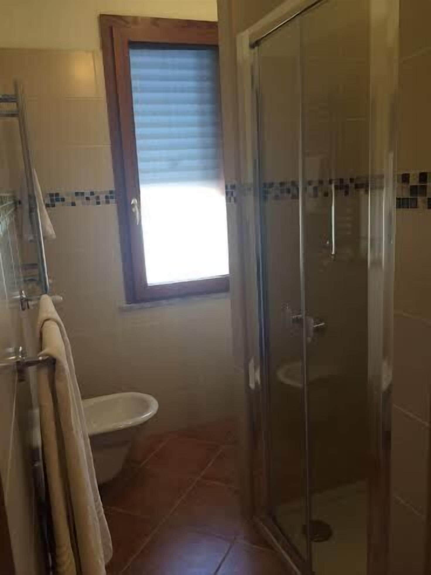 Ein Badezimmer mit Duschkabine aus Glas, Toilette und einem Fenster mit Jalousien.