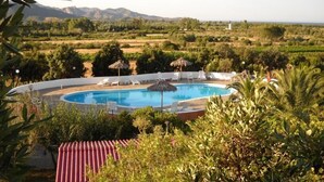 Piscina rodeada de sillas de descanso y sombrillas, con vistas a un paisaje rural y montañas al fondo.