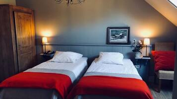 A hotel room with two beds, a chandelier, a framed picture on the wall, and a nightstand with a lamp.