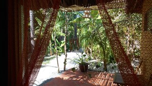 A covered outdoor area with a tiled floor, surrounded by plants and a pergola structure. - Thuy - Gunter Garden Bungalow (Mui Ne)