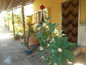 A covered outdoor area with a table and chairs, a potted plant, and a door with a decorative screen. - Thuy - Gunter Garden Bungalow (Mui Ne)