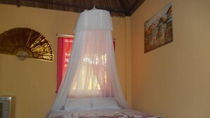 A bed with a canopy, a wall fan, a painting, and a red curtain. - Thuy - Gunter Garden Bungalow (Mui Ne)