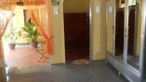 A hotel lobby with a tiled floor, a wooden chair, a potted plant, and a glass door with a metal frame. - Thuy - Gunter Garden Bungalow (Mui Ne)