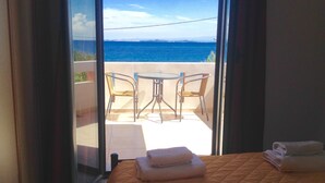 Una habitación con cama, una mesita, dos sillas y vista al mar a través de un ventanal.