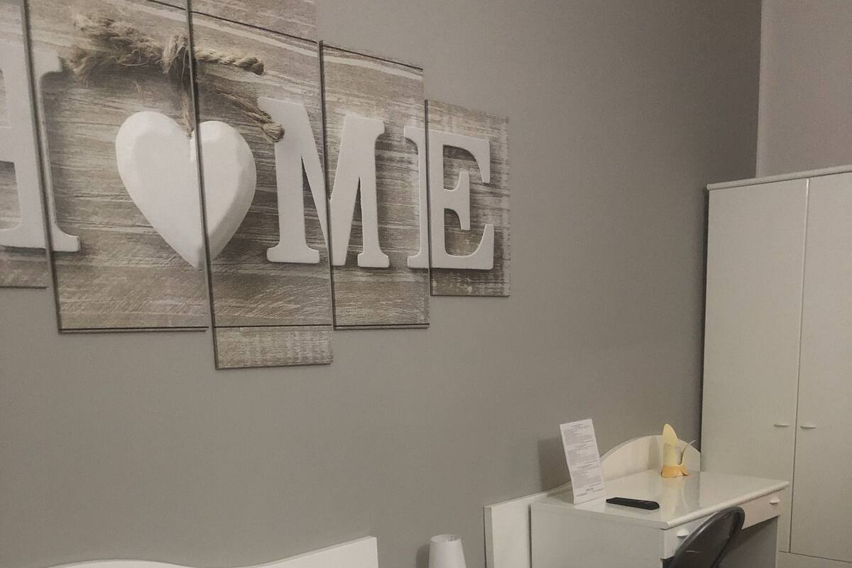 A hotel room with a bed, a desk, a wardrobe, and a wall with a 'HOME' sign.