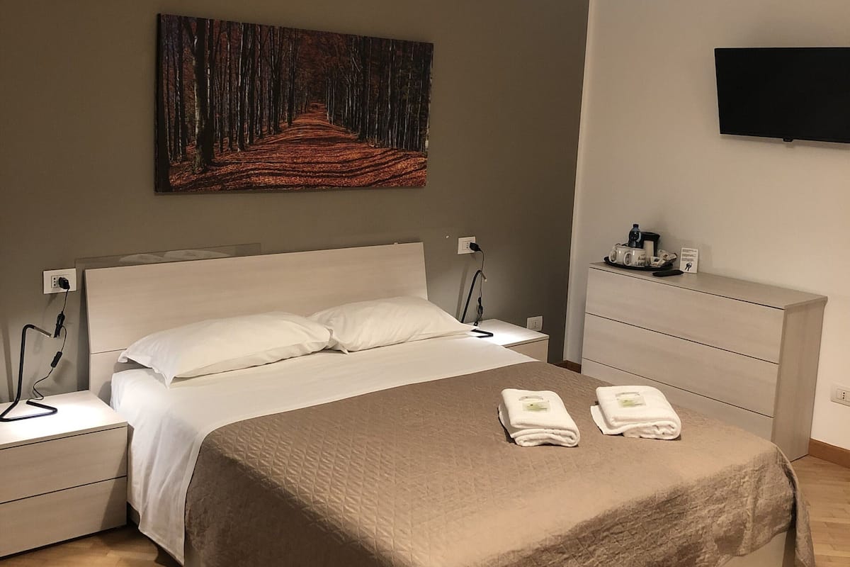 A neatly arranged hotel room with a bed, bedside tables, a flat-screen TV, and a painting on the wall.