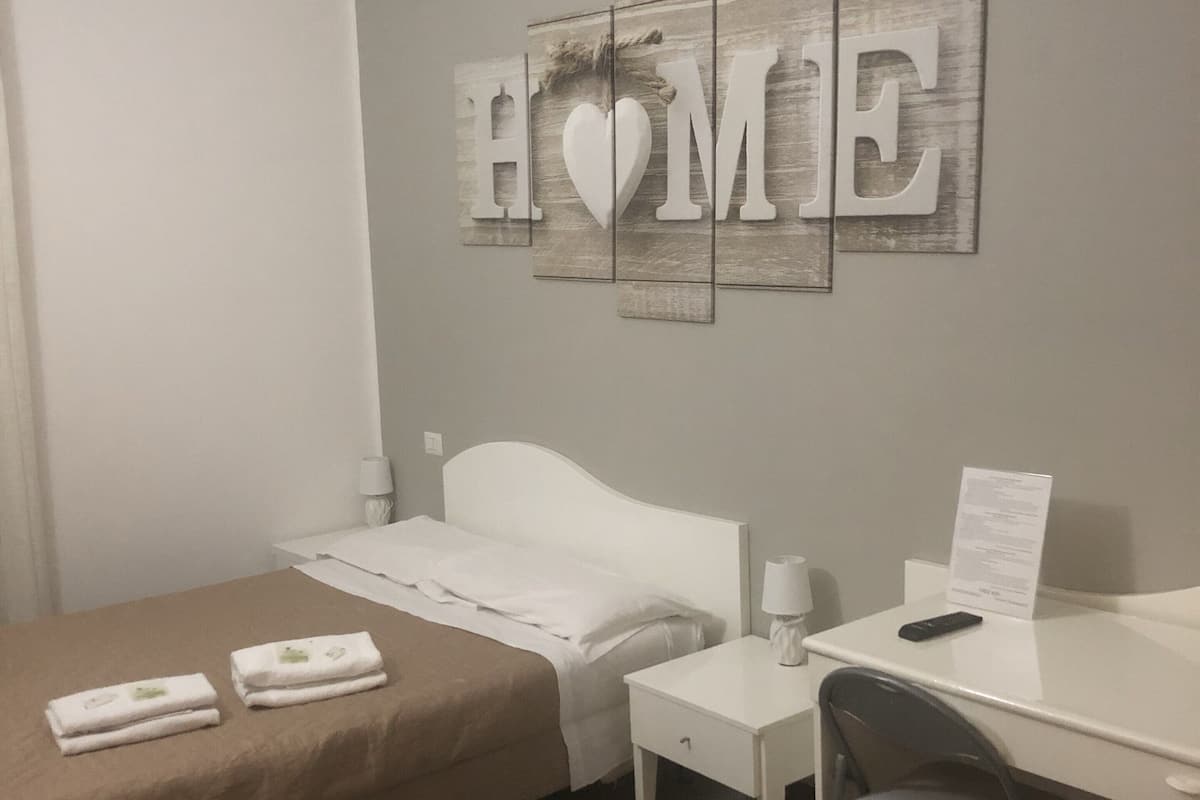 A hotel room with a bed, a desk, a chair, and a wall decoration spelling "HOME".