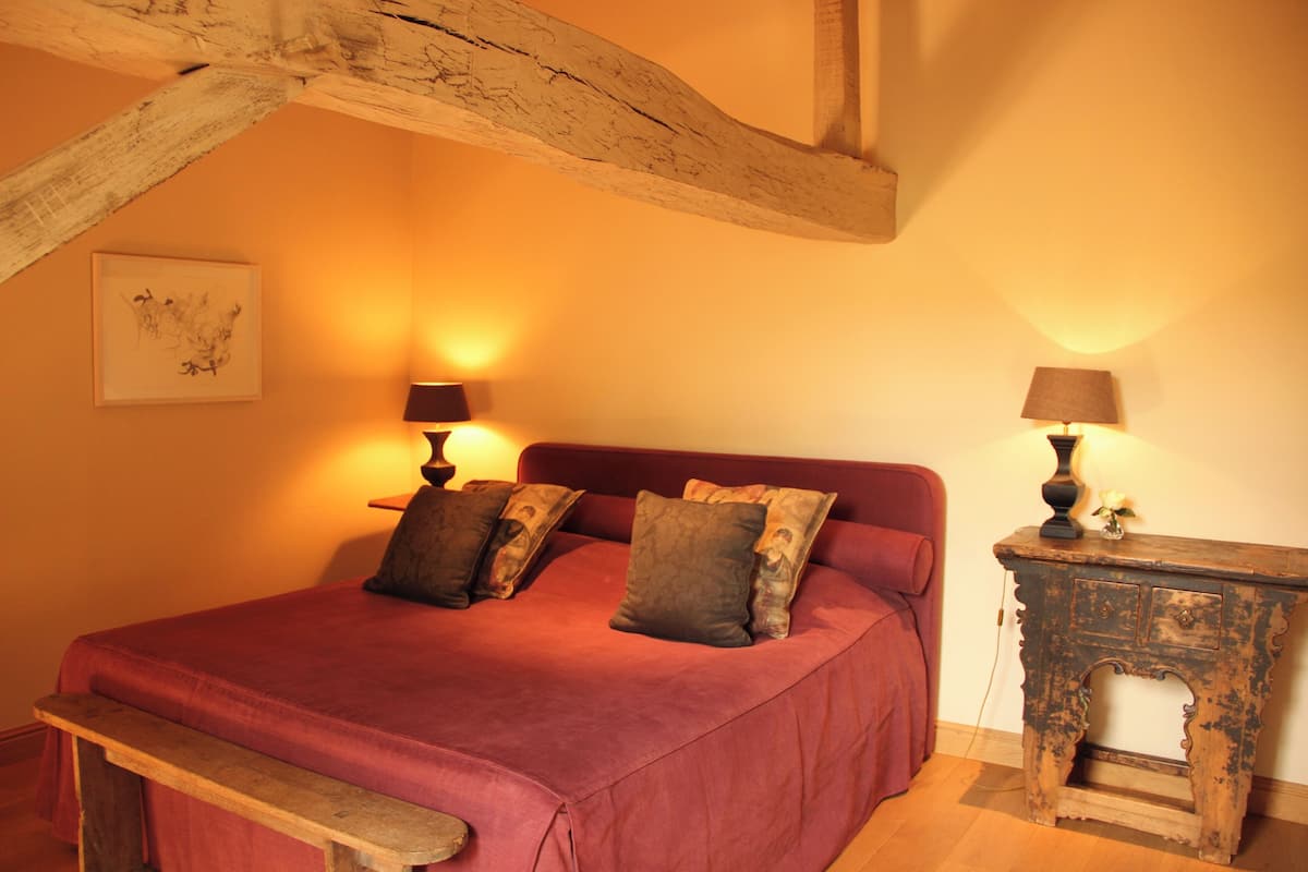 A bedroom with a wooden bed frame, a red bedspread, and two bedside lamps.