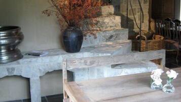 Un interior rústico con un banco de piedra, una mesa de madera y un jarrón con flores rojas.
