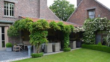 Een bakstenen huis met een overdekte patio, buitenzitplaatsen en een verzorgd gazon.