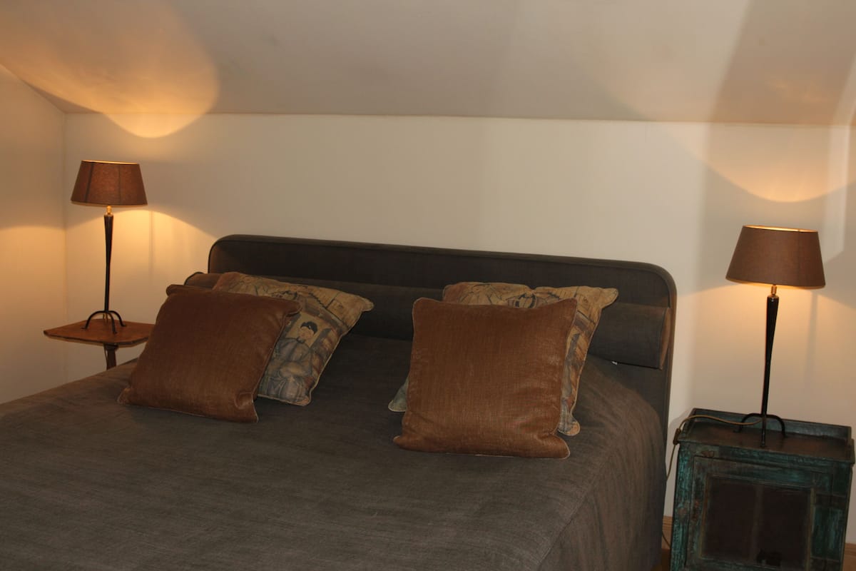A bed with a dark headboard, two brown pillows, and a matching blanket. There are two bedside tables with lamps on either side of the bed.