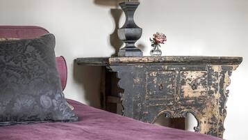 Una cama con colcha morada, una mesita de noche con lámpara y un objeto decorativo sobre la mesa.