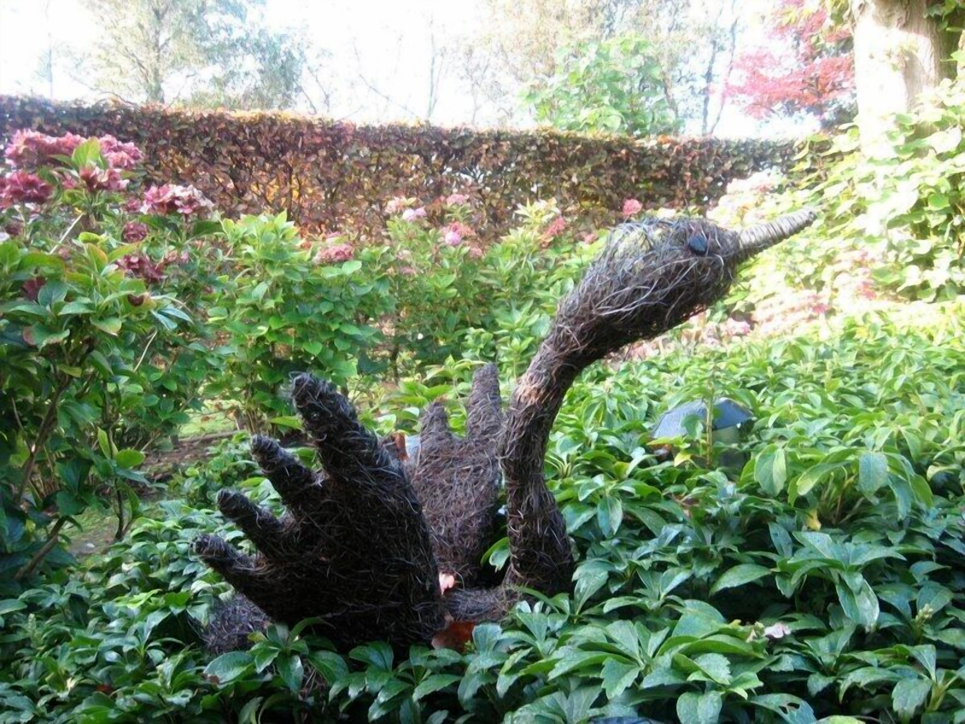 A garden with a sculpture of a hand reaching upwards amidst lush greenery and flowering plants.