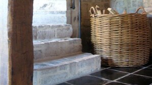 Una escalera con escalones de piedra y barandal de madera que conduce a una habitación con pared de piedra y una cesta tejida en el suelo.