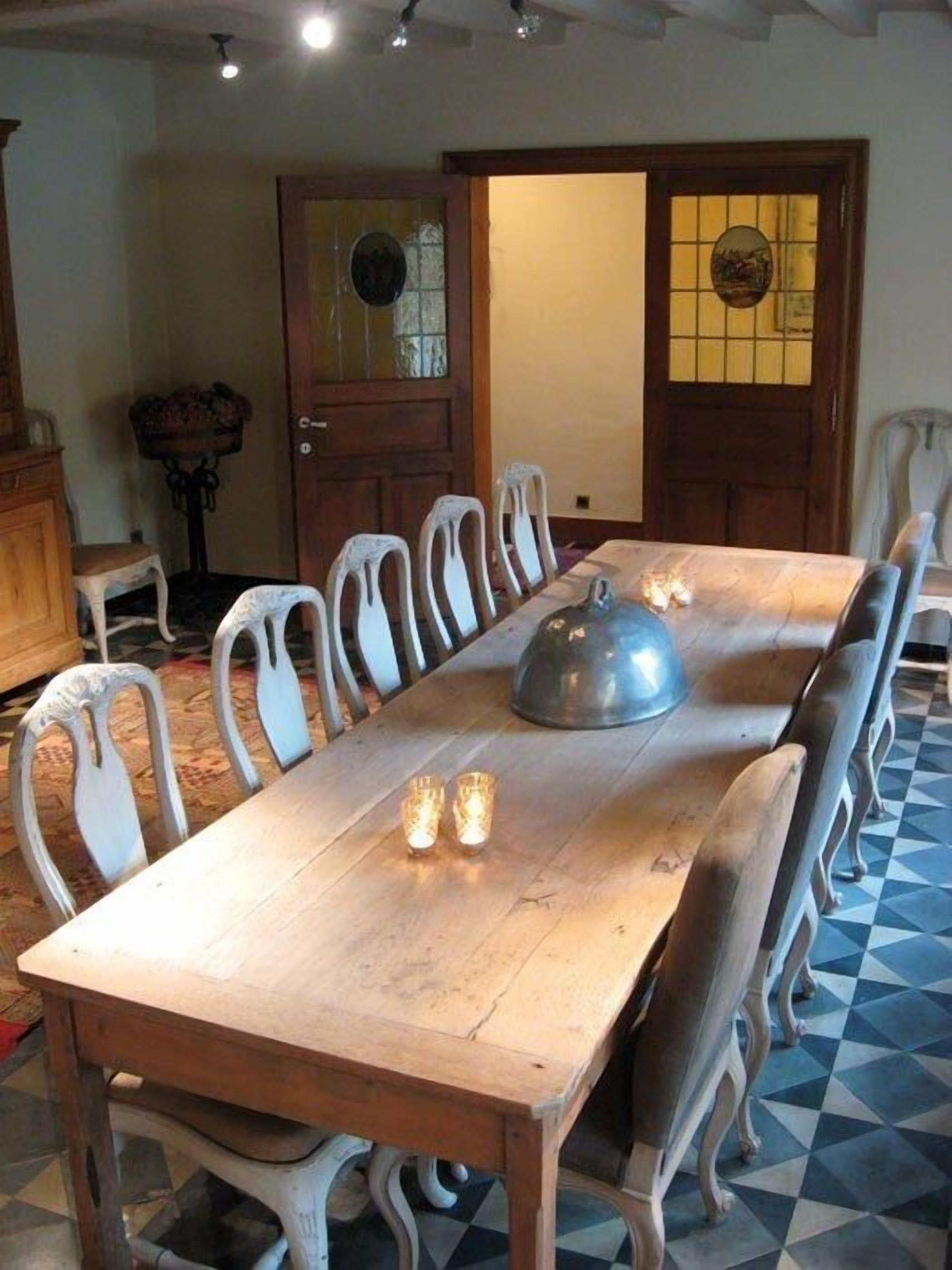 Comedor con mesa de madera, sillas blancas y un recipiente metálico grande para servir.