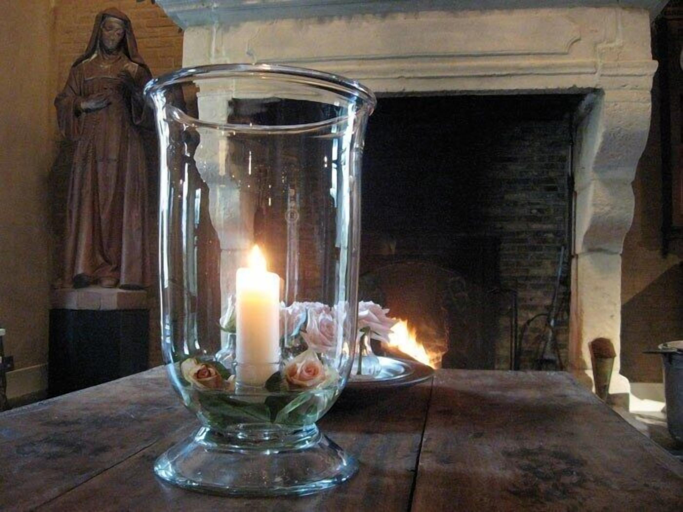 A clear glass candle holder with a lit candle and roses on a wooden table.