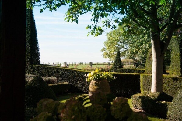 Un jardín bien cuidado, con setos recortados, un gran árbol y un muro de piedra.