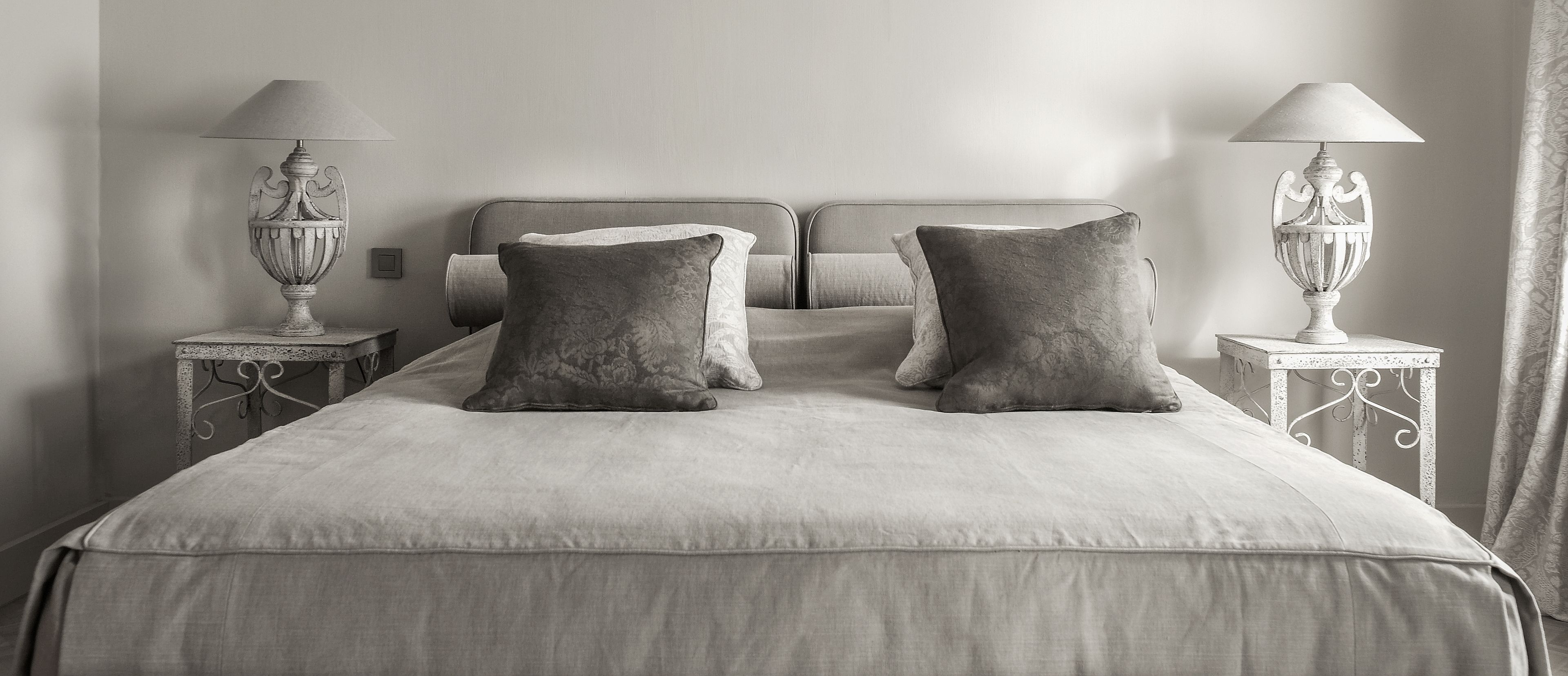 A neatly made bed with two large pillows and two bedside lamps on matching nightstands.