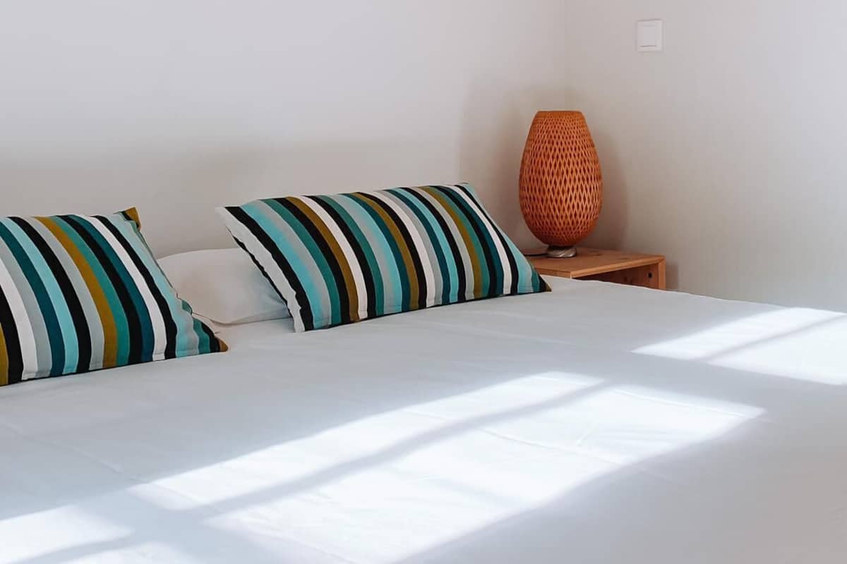 Ein Schlafzimmer mit einem Bett, zwei gestreiften Kissen, einem kleinen Nachttisch und einer gewobenen Lampe.