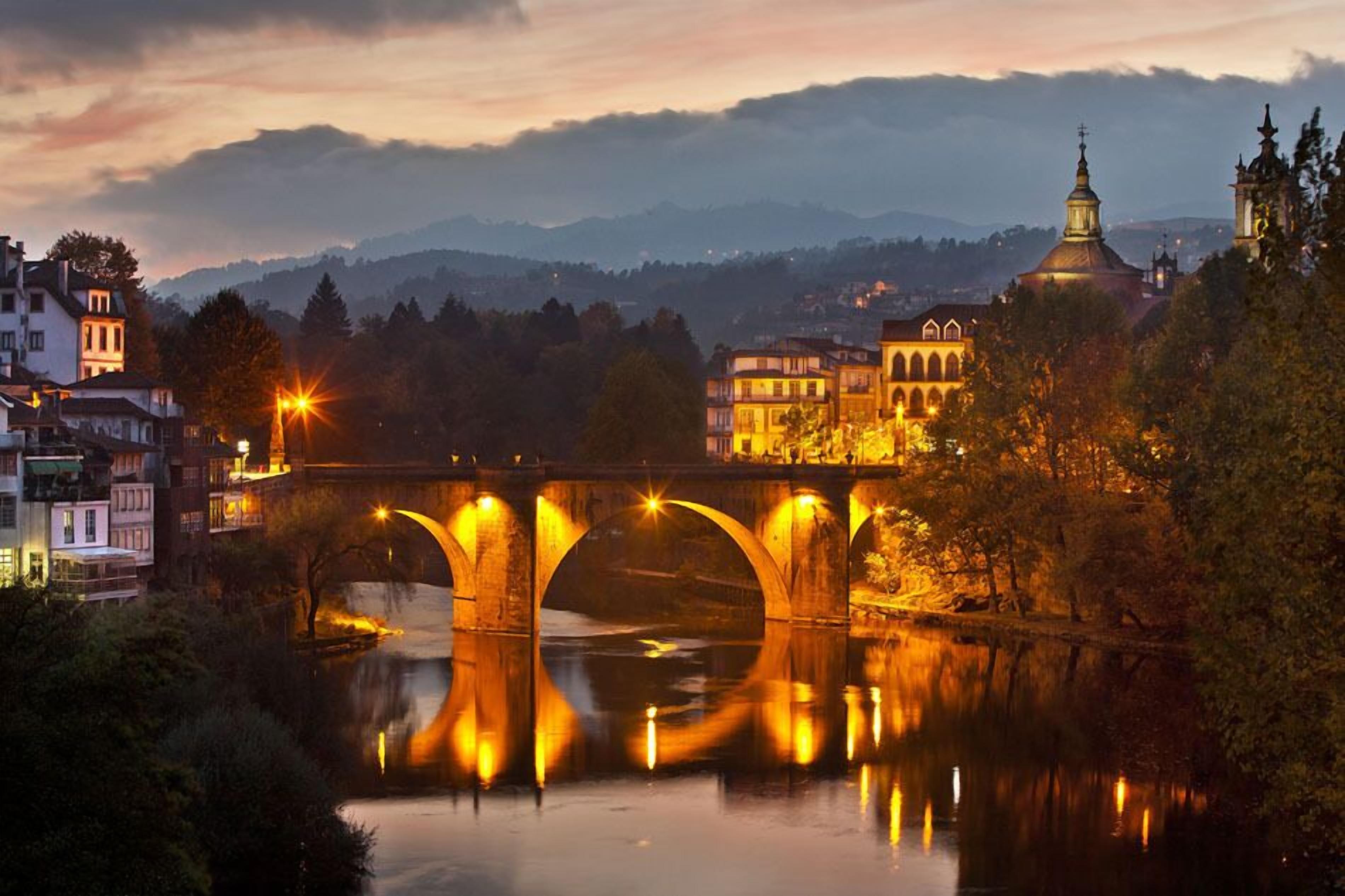 Un puente de tres arcos sobre un río, rodeado de edificios y una iglesia con cúpula.