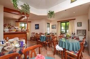 A dining area with wooden chairs and tables, a buffet setup, and hanging plants. - Apollon Hotel (Naxos)