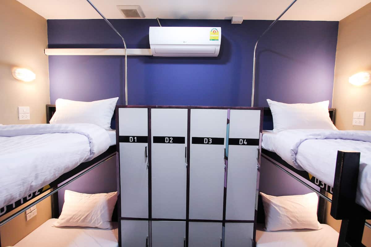 A hotel room with bunk beds, a wardrobe with numbered compartments, and an air conditioning unit on the wall.