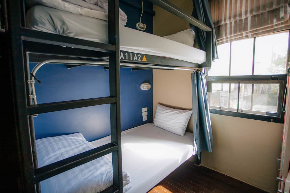 A bunk bed room with a window, a curtain, and a wall socket.