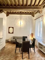 Zona pranzo con tavolo rotondo, quattro sedie, una poltrona e un lampadario a parete.
