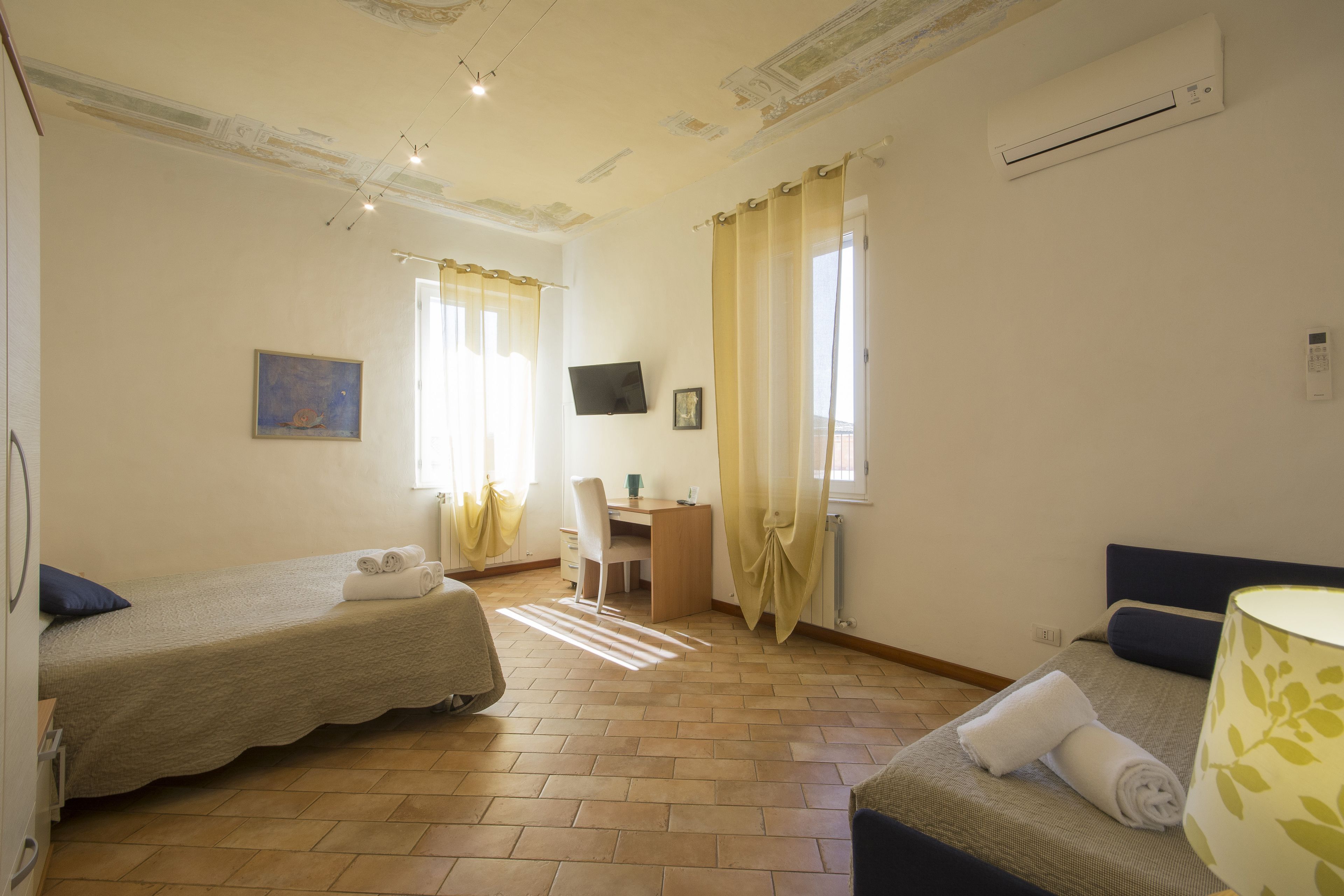 Ein Hotelzimmer mit zwei Einzelbetten, einem Schreibtisch, einem Stuhl, einem Fernseher und einer Klimaanlage.