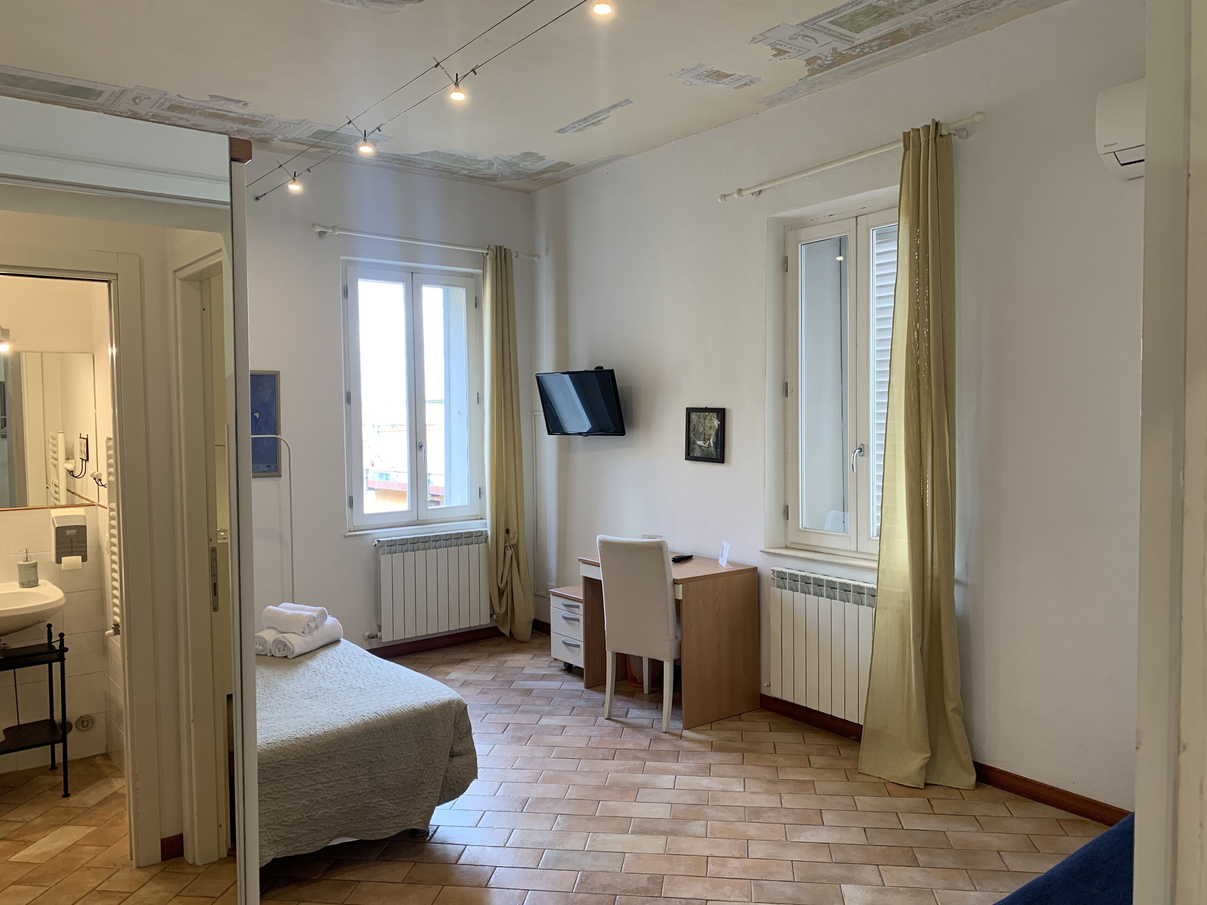 Un dormitorio con cama, escritorio, silla, televisión y ventana con cortinas.