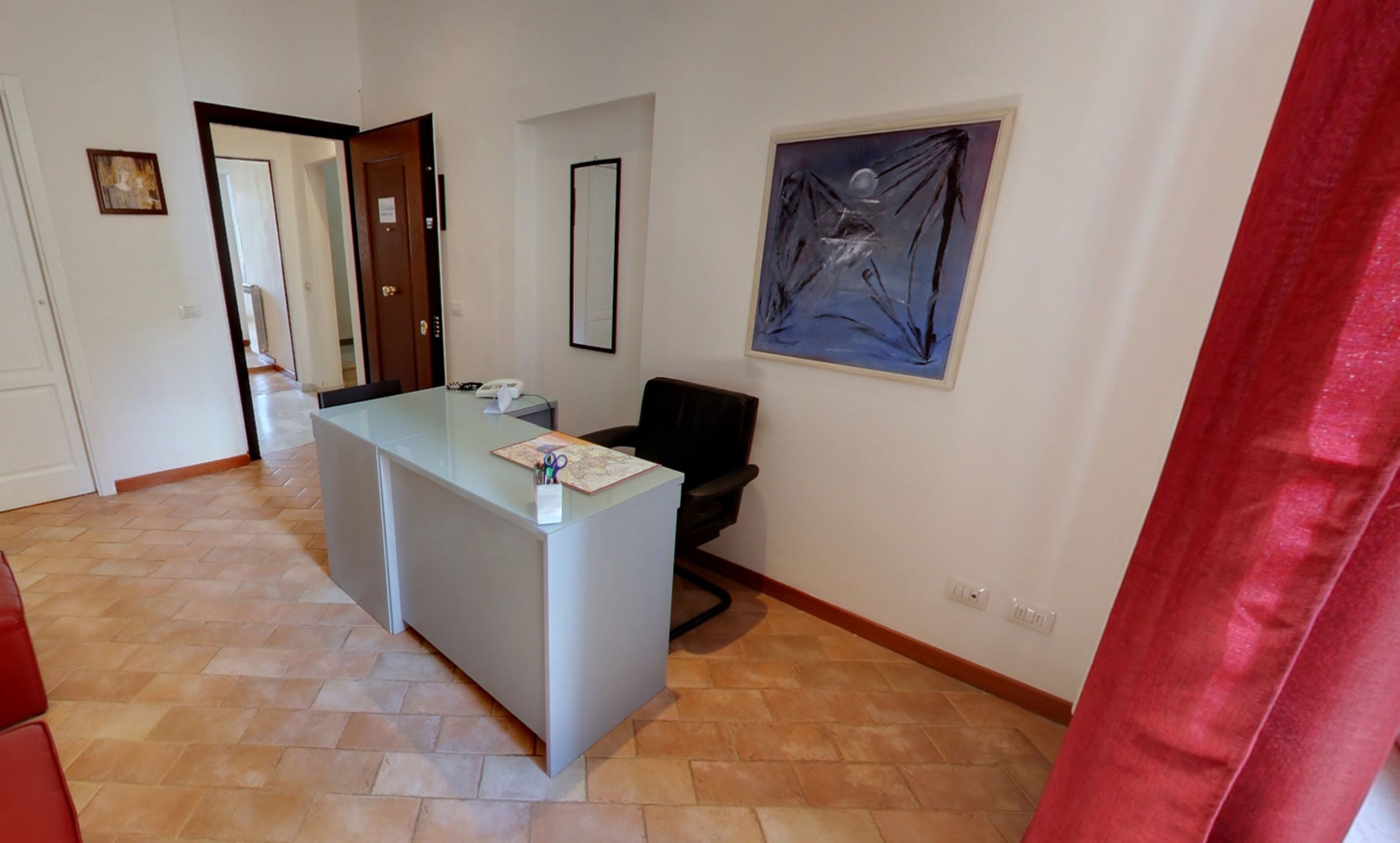 Un'area reception con una scrivania in vetro, una sedia da ufficio nera e un quadro appeso al muro.