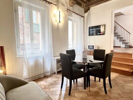 Un soggiorno moderno con un tavolo in vetro e quattro sedie, una TV a schermo piatto montata sulla parete e una scala che conduce a un piano superiore.