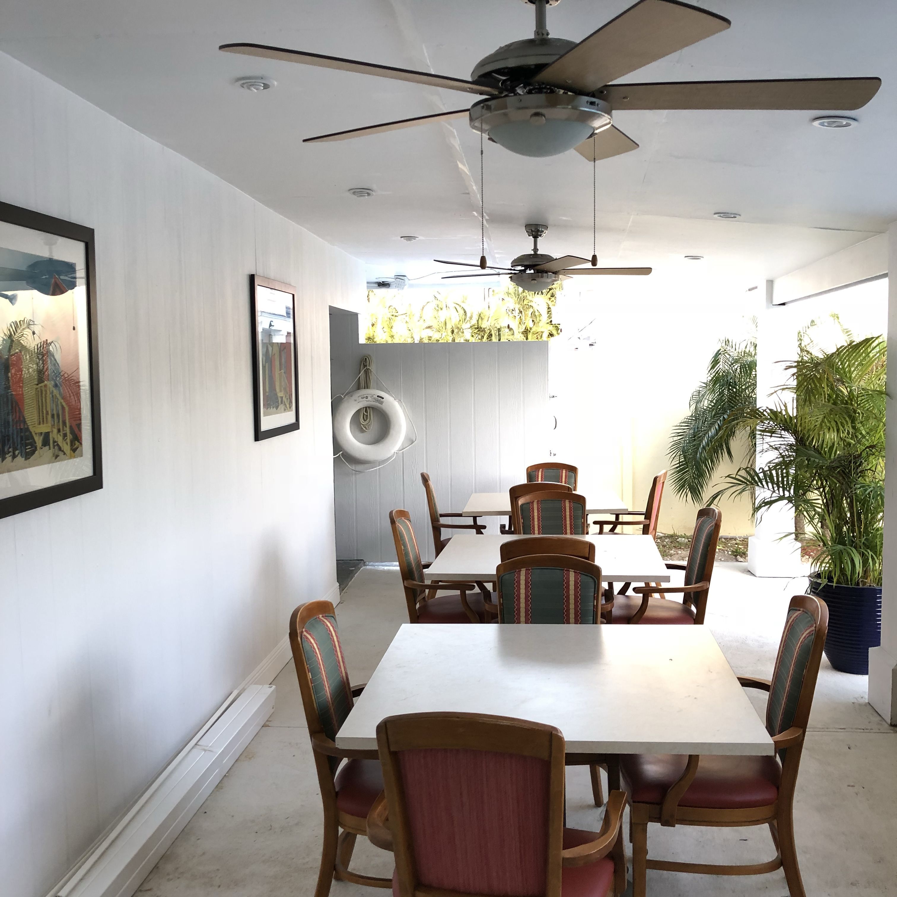 A dining area with a white table and chairs, a ceiling fan, and a view of the outdoors.