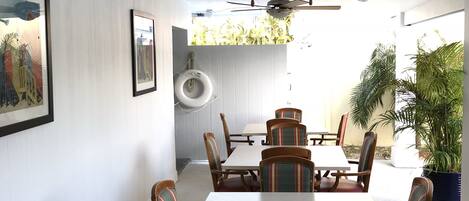A dining area with a white table and chairs, a ceiling fan, and a view of the outdoors.