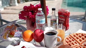 Una mesa de desayuno con huevos, salchichas, croissants, gofres, jugo, café, kétchup, mostaza y agua.
